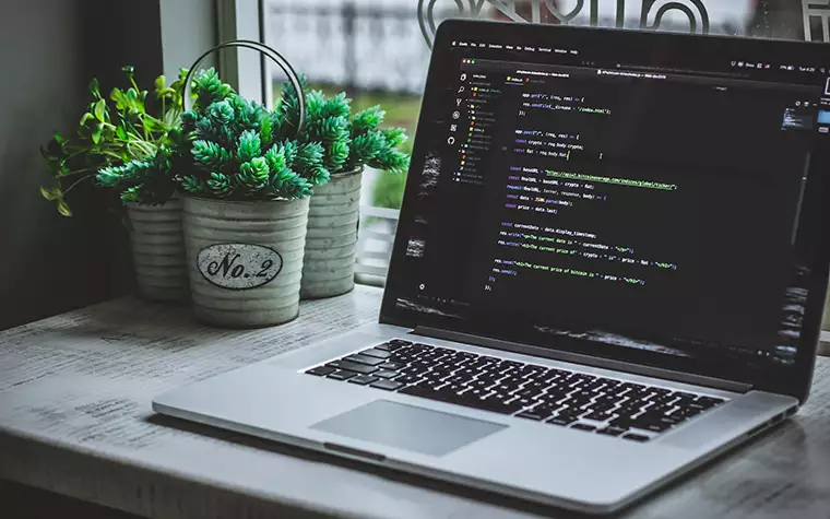 A laptop infront of a window that shows coding and programming