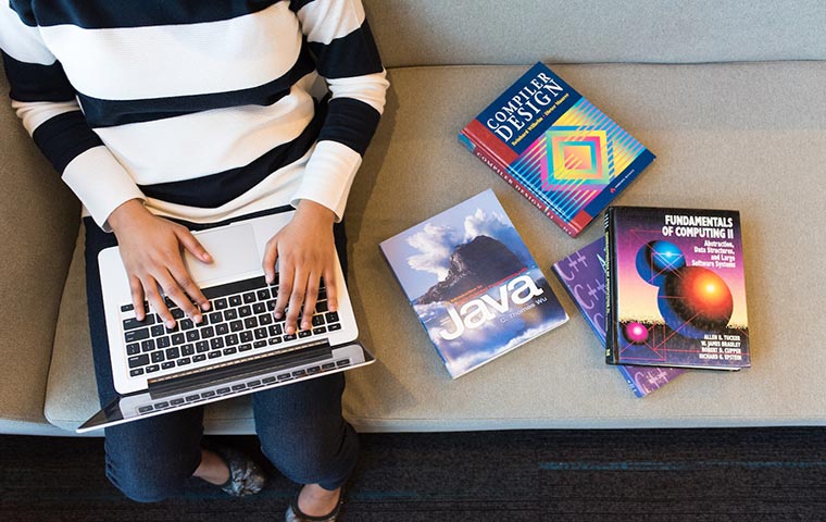 A man is working with his laptop with books of coding and front end languages